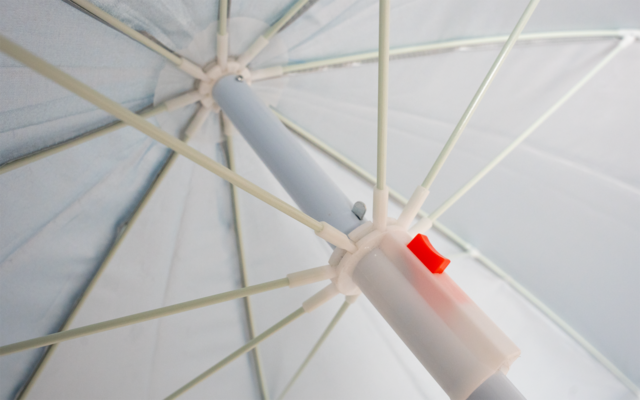 Innenseite eines weißen Sonnenschirms mit Metallstreben, zentralem Mast und rotem Verriegelungsriegel