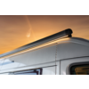 Partie supérieure d'un camping-car blanc avec un store fermé fixé au bord du toit, ciel orange en arrière-plan