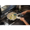 Dos manos sujetan unas pinzas de cocina sobre una sartén con rodajas de calabacín en aceite en una cocina de gas; fregadero y encimera visibles al fondo