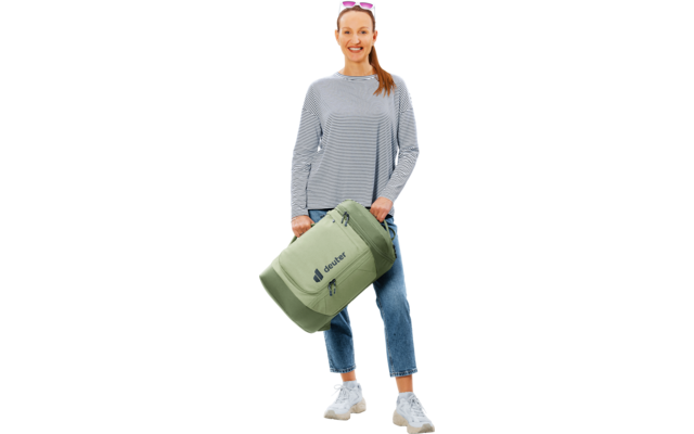 Frau in gestreiftem Langarmshirt, Jeans und weißen Sneakern, steht und hält eine hellgrüne Reisetasche mit 'deuter'-Logo
