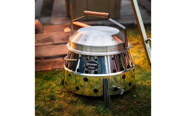 Rundes Metallgerät mit Deckel, Holzgriff, Standfüßen und Lüftungsöffnungen auf Gras