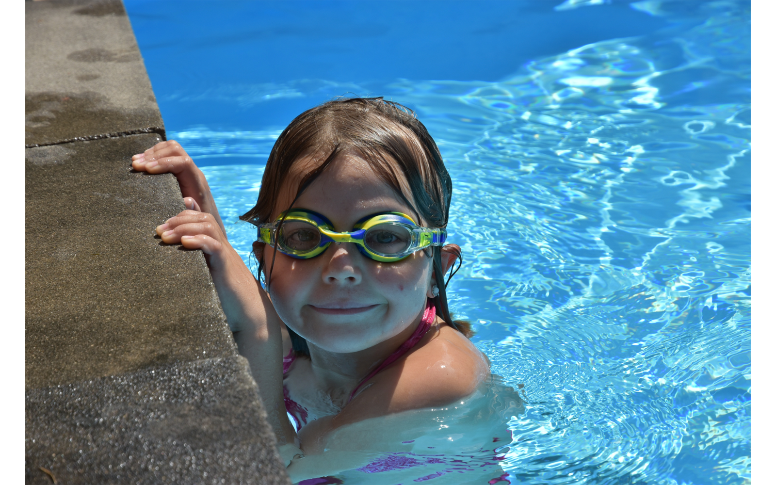 Kind mit Schwimmbrille im Wasser neben einem Poolrand