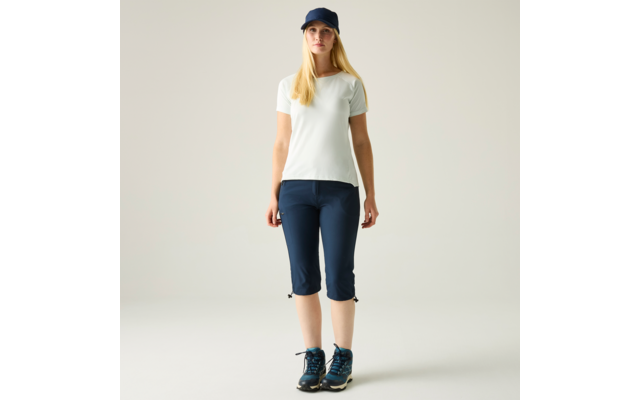 Person steht frontal vor hellem Hintergrund, trägt weißes T-Shirt, blaue Kappe, blaue Dreiviertelhose und blaue Wanderschuhe