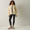 Persona in piedi davanti a uno sfondo neutro che indossa una giacca in pile color crema con cerniera, un top nero, leggings neri, calzini e scarpe da ginnastica beige