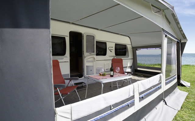 Weiße Markise über einer Terrasse mit Stühlen vor einem Wohnwagen