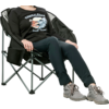 Femme assise détendue dans une chaise pliante, portant des vêtements noirs et des baskets grises