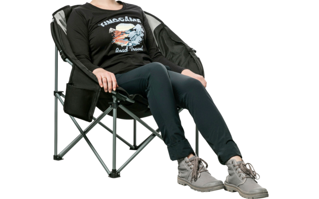 Femme assise détendue dans une chaise pliante, portant des vêtements noirs et des baskets grises