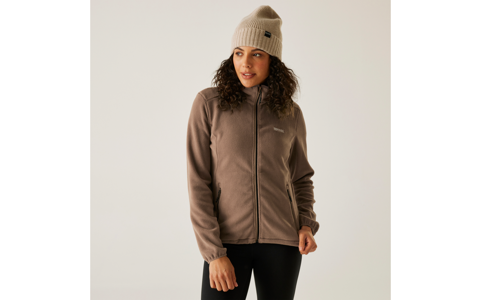 Vrouw met een bruine jas en een beige muts voor een witte achtergrond