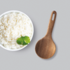 Weiße Schüssel mit Reis und grünem Kraut daneben ein Holzlöffel auf grauem Hintergrund