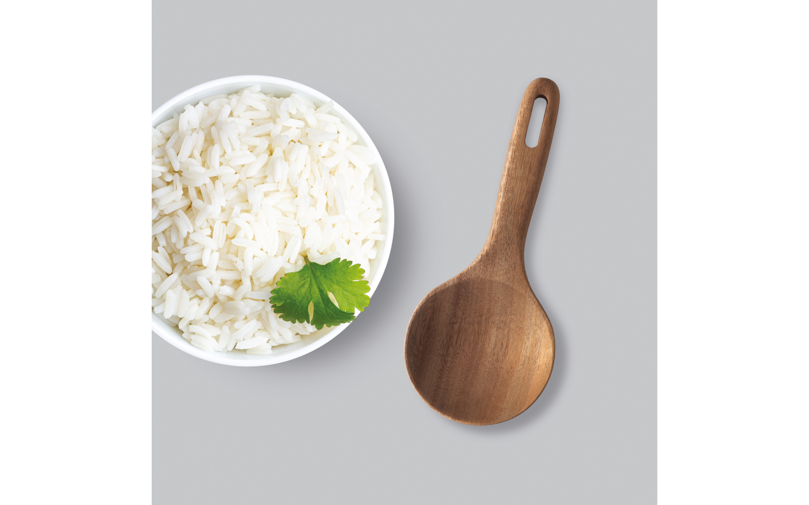 Weiße Schüssel mit Reis und grünem Kraut daneben ein Holzlöffel auf grauem Hintergrund