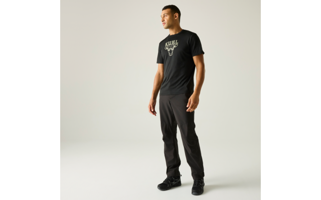 Mann steht, schwarzes T-Shirt mit Stier-Logo, schwarze Hose, schwarze Schuhe, heller Hintergrund