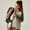 Woman with red ponytail wearing a quilted outdoor jacket and backpack, holding the zipper and looking down while smiling