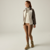 Person standing on a light background, wearing a light beige-grey hooded jacket, light sweater, brown leggings and beige hiking boots, hair in a ponytail