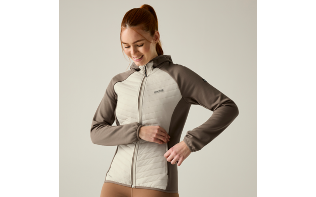 Person with red hair in a ponytail wearing a two-tone quilted zip jacket, smiling and looking down while adjusting the zipper, on a light neutral background