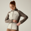 Person with red hair in a ponytail wearing a two-tone quilted zip jacket, smiling and looking down while adjusting the zipper, on a light neutral background
