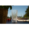 Doorzichtig, gestructureerd drinkglas op een donkere tafel; links een gevlochten bloempot en twee cherrytomaten; rechts een onscherpe kom met groene voorwerpen; onscherpe blauwe lucht op de achtergrond