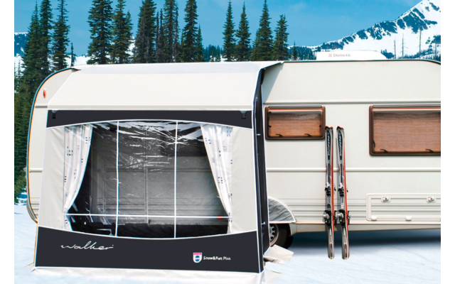 Wohnwagen mit angebautem Vorzelt in einer schneebedeckten Landschaft, im Hintergrund Bäume und Berge