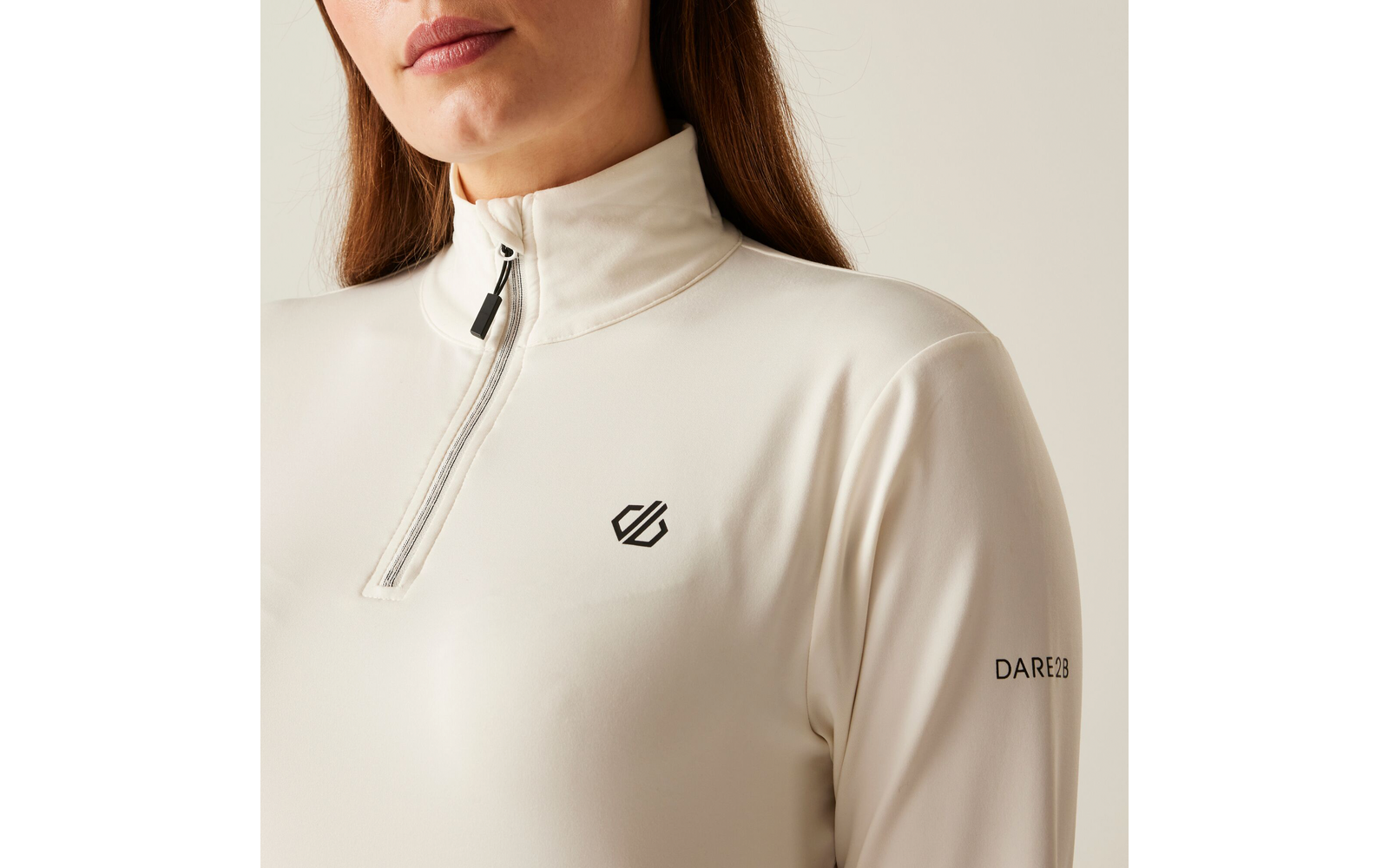 Femme portant un pull à col roulé beige clair avec fermeture éclair et logo sur la poitrine