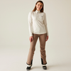 Femme debout devant un fond clair, porte une veste sweat claire et un pantalon beige