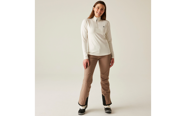 Femme debout devant un fond clair, porte une veste sweat claire et un pantalon beige