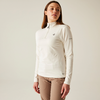Femme aux longs cheveux bruns portant un pull à col roulé blanc et un pantalon marron, debout devant un fond clair