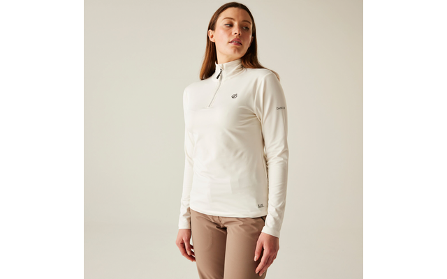 Femme aux longs cheveux bruns portant un pull à col roulé blanc et un pantalon marron, debout devant un fond clair