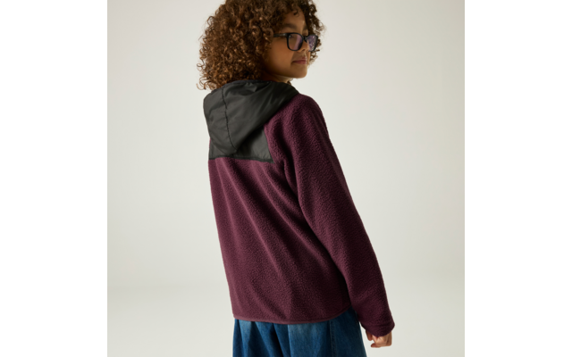 Person von hinten mit lockigem Haar und Brille, trägt dunkelviolette Fleecejacke mit schwarzer Kapuze, schaut über die Schulter
