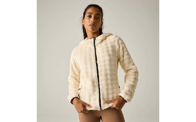 Persona con el cabello recogido que lleva una chaqueta con capucha de pelo sintético color crema con cremallera negra y leggings marrón claro sobre fondo claro