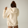Persona vista de espaldas con chaqueta con capucha de piel sintética color beige claro, tirando de la capucha; cabello castaño recogido; fondo liso claro