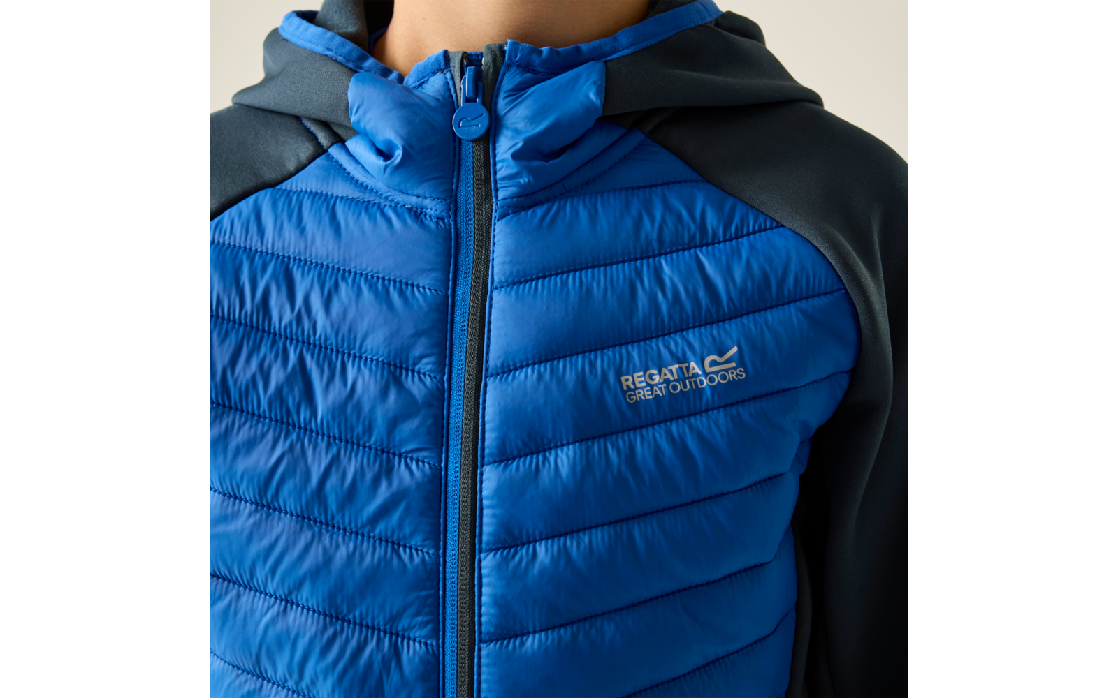 Brustbereich einer Person in einer blauen gestepp­ten Jacke mit Reißverschluss, dunkelblauen Ärmeln und dem Logo 'Regatta Great Outdoors' auf der Brust