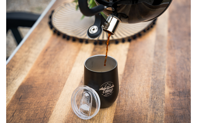 Koffie wordt vanuit een apparaat in een zwarte beker op een houten tafel gegoten