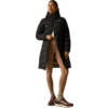 Persona con cappotto imbottito nero lungo, leggings beige e scarpe da ginnastica marroni, in piedi con una mano sulla cerniera, sguardo in alto a destra, sfondo chiaro