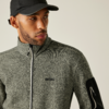 Ein Mann mit schwarzer Kappe und grauem Pullover vor hellem Hintergrund