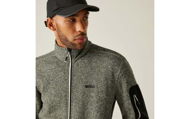 Ein Mann mit schwarzer Kappe und grauem Pullover vor hellem Hintergrund