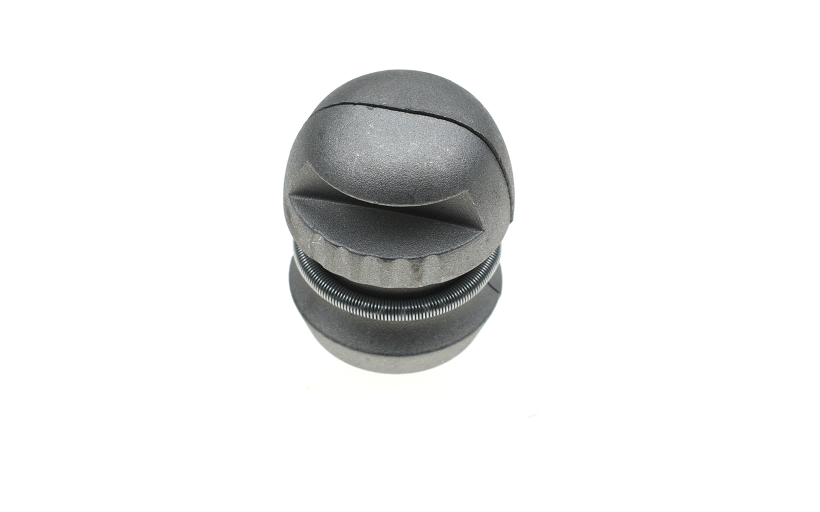 Graues zylindrisches Objekt aus zwei gestapelten, abgerundeten Scheiben; obere Scheibe mit gebogener Schlitzöffnung; zwischen den Scheiben sichtbare Metallspiralfeder; weißer Hintergrund