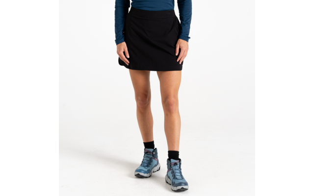 Onderlichaam van een staande persoon met een zwarte rok, blauw shirt met lange mouwen, zwarte sokken en blauwe wandelschoenen tegen een witte achtergrond