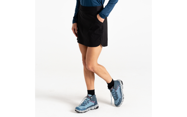 Onderlichaam van een staande persoon, met een korte zwarte rok met zijzak, een blauw top met lange mouwen, zwarte sokken en blauwe wandelschoenen op een witte achtergrond