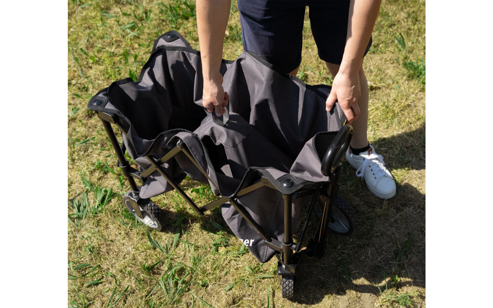 Person faltet schwarzen zusammenklappbaren Stuhl auf einer Grasfläche auf