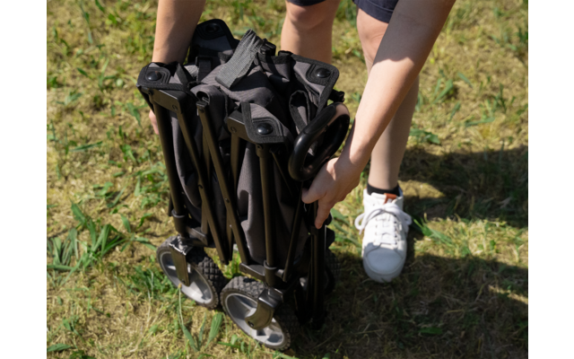 Person faltet ein schwarzes, tragbares Stuhlgestell auf einer grünen Wiese zusammen