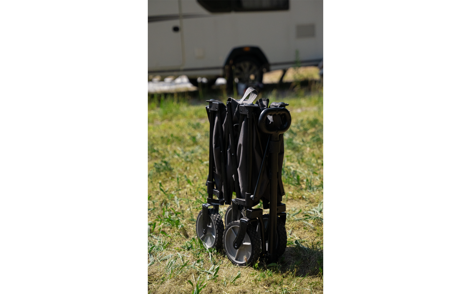 Zusammengeklappter schwarzer Buggy steht auf Gras vor einem weißen Anhänger