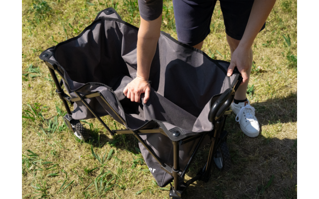 Person faltet ein dunkles faltbares Outdoor-Möbelstück auf einer Wiese auf