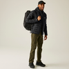 Mann trägt schwarze Jacke, schwarze Mütze, grüne Hose und schwarzen Rucksack