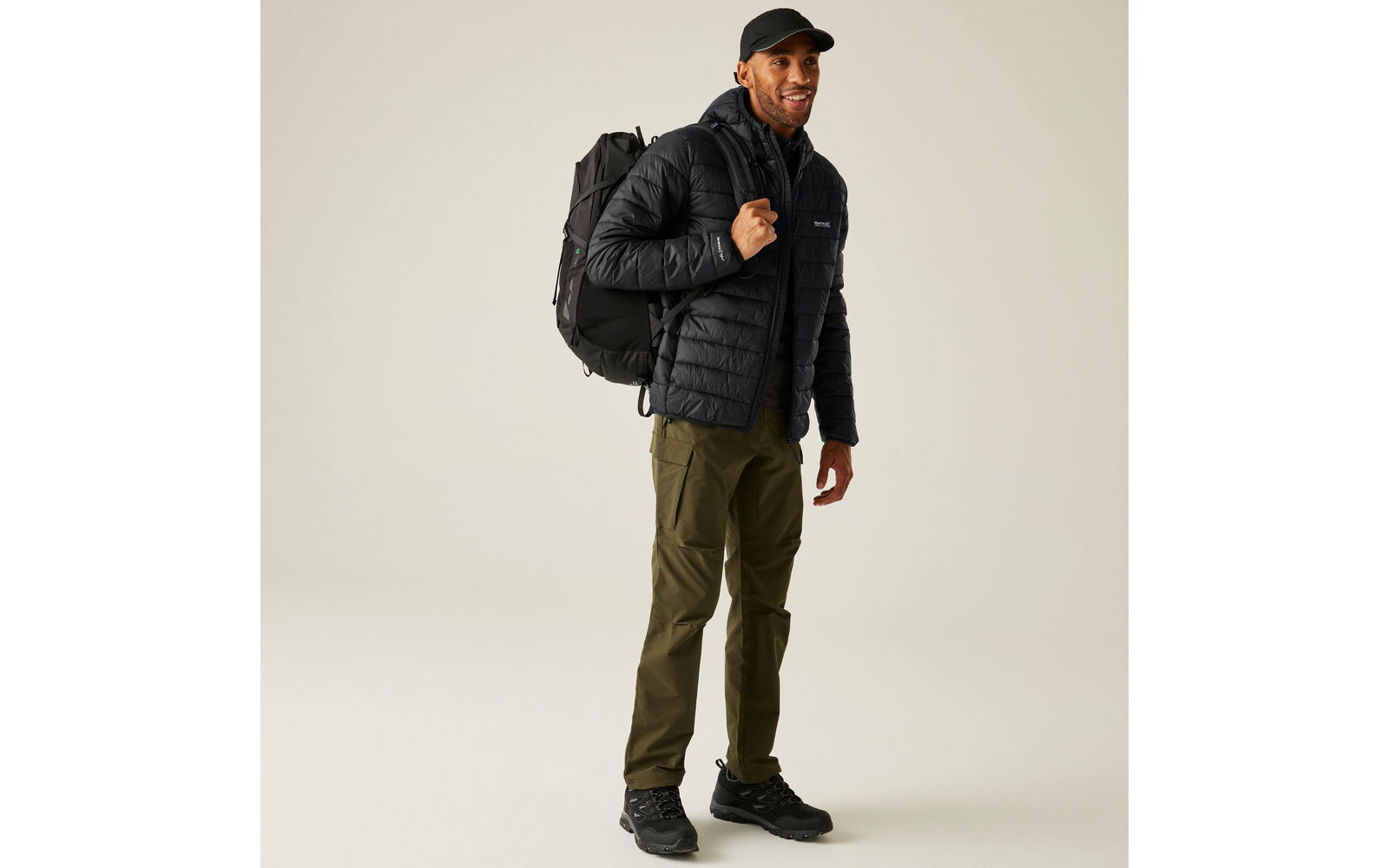 Mann trägt schwarze Jacke, schwarze Mütze, grüne Hose und schwarzen Rucksack