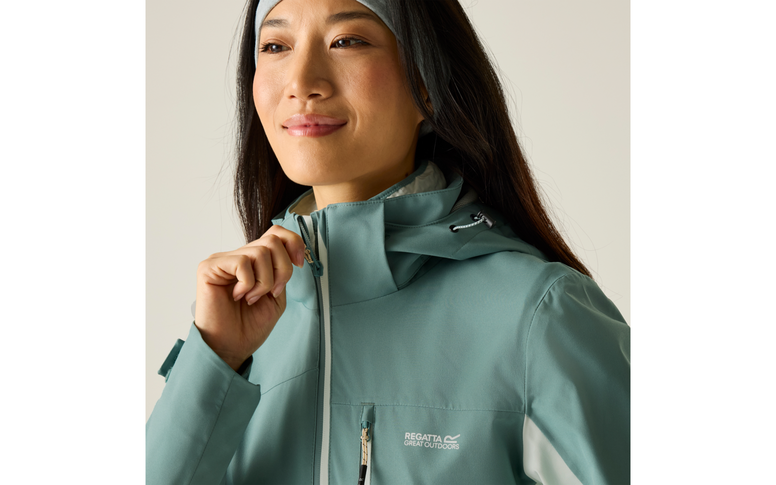 Nahaufnahme einer Person mit langem dunklem Haar, die am Reißverschluss einer türkisgrünen Outdoorjacke mit Kapuze zieht; 'Regatta Great Outdoors'-Logo sichtbar
