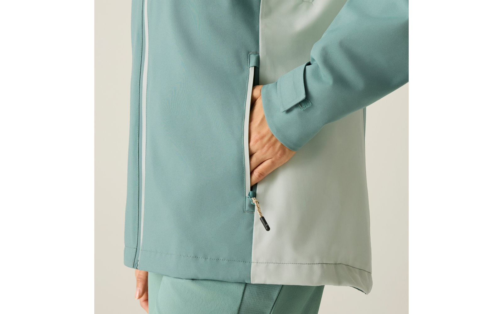Nahaufnahme: Hand steckt in Reißverschlusstasche einer zweifarbigen türkisgrünen Jacke; Ärmel und Teil der Hose sichtbar