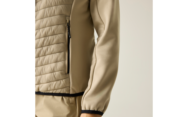 Nahaufnahme einer hellbeigen, gesteppten Jacke mit Reißverschlusstasche, Ärmel, schwarzem Saum und passender hellbeiger Hose vor neutralem Hintergrund