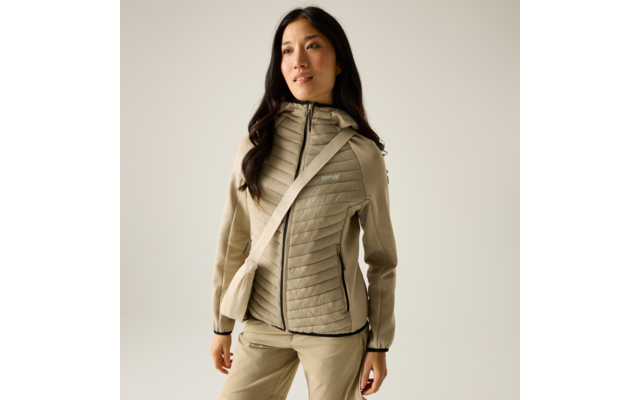 Person trägt beige gesteppte Kapuzenjacke, passende Hose und Umhängetasche; steht vor hellem einfarbigem Hintergrund, Blick leicht nach rechts