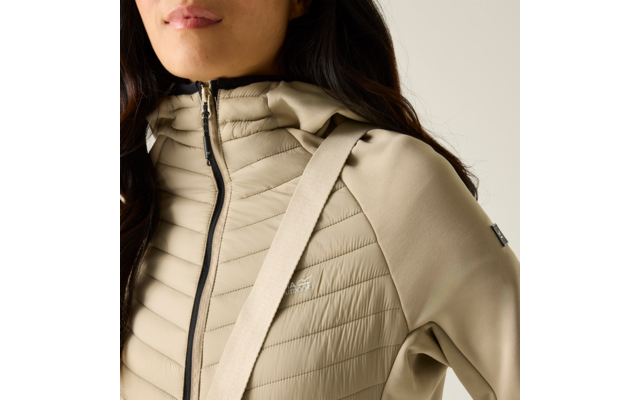 Brustansicht einer Person in beiger Steppjacke mit Reißverschluss, hohem Kragen und diagonalem Träger über der Schulter; dunkle Haare sichtbar