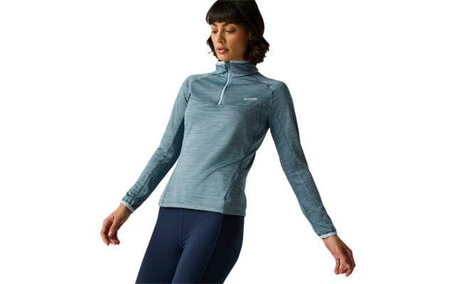 Personne aux cheveux courts et foncés avec frange, portant un haut bleu clair à manches longues avec demi-fermeture éclair au col et petit logo sur la poitrine, et des leggings bleu foncé, debout devant un fond clair et regardant vers le bas