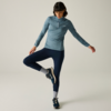 Personne aux cheveux foncés jusqu'aux épaules, haut bleu à manches longues avec courte fermeture éclair, legging bleu marine, chaussettes blanches et baskets bleues, debout sur une jambe devant un fond clair, regard vers le bas
